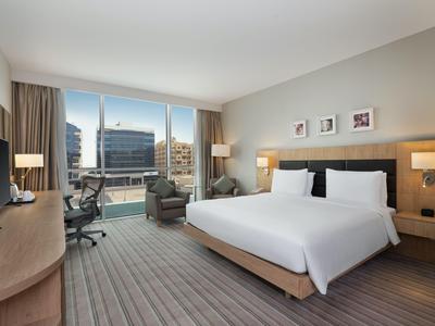 Modern hotel room with large bed, seating area, and panoramic window overlooking the city.