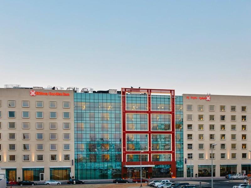 Modern hotel building with glass facade and parking spaces in front under clear sky