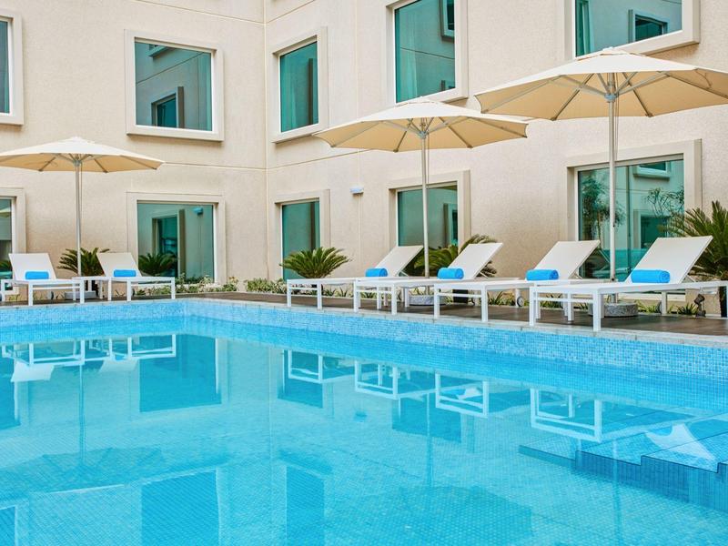 Clear swimming pool with loungers and umbrellas in front of a hotel building.