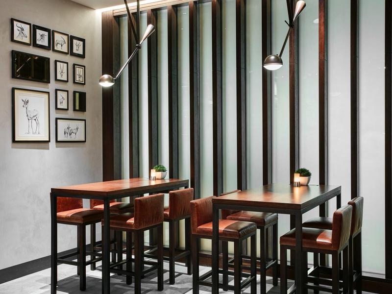 Modern dining area with wooden chairs, tables, and gallery wall in daylight.