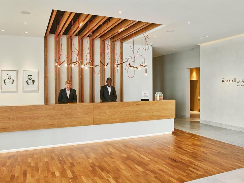 Modern hotel reception with light wood and two receptionists.