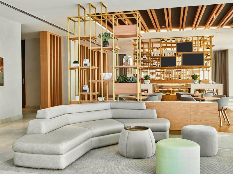 Modern hotel lobby with a curved gray sofa and open bar in the background.