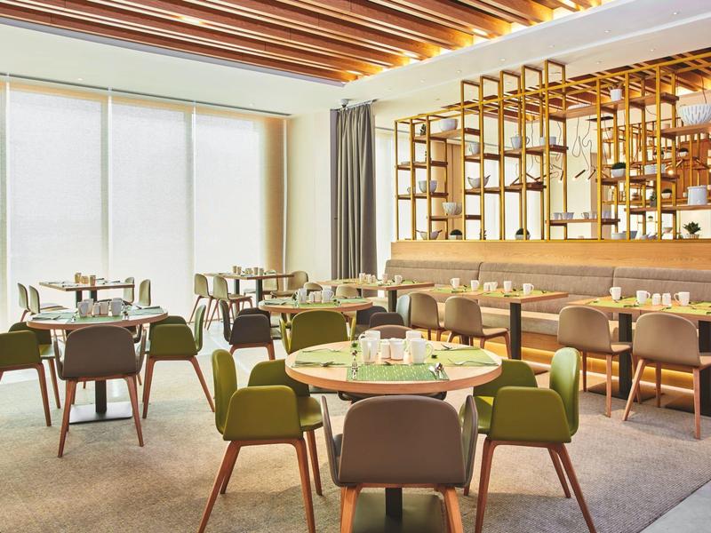 Modern hotel restaurant with green chairs and large windows letting in natural light.