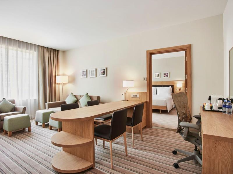Modern hotel room with desk, chairs, and large window with curtains.