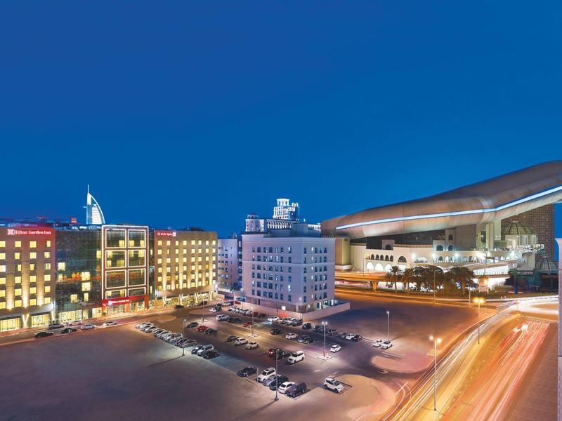 Illuminated hotel and event hall at night with parking lot and clear blue sky.