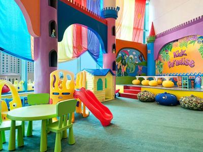Aire de jeux colorée pour enfants avec toboggan, coussins doux et petites tables dans un hôtel.