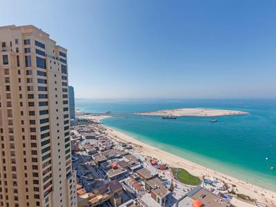 Blick auf hohe Gebäude, Strand mit hellem Sand und türkisblaues Meer unter klarem Himmel.