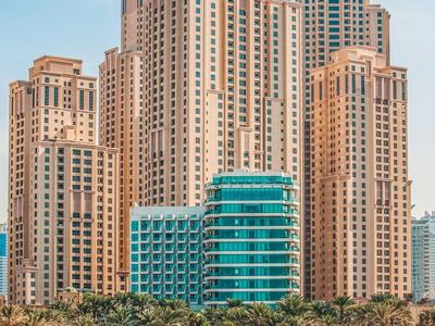 Plusieurs grands bâtiments modernes au bord d'une plage avec une mer bleue et un ciel clair.