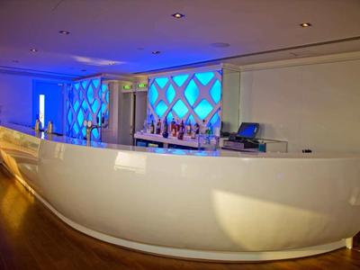Moderner, geschwungener weißer Hotelbar-Tresen mit blauer Beleuchtung im Hintergrund.