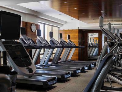 Helle Fitnessstudio mit laufenden Bändern und Cardiogeräten vor großen Fenstern