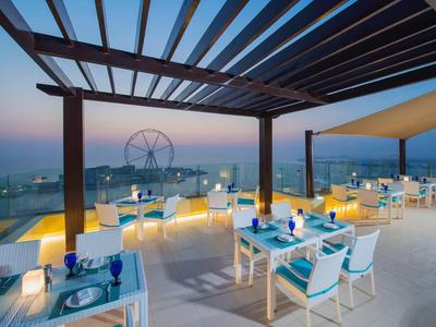 Terrasse de restaurant avec pergola, tables, chaises et vue sur la mer au coucher du soleil.