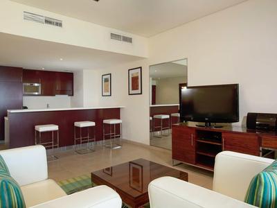 Salon moderne avec TV, meubles en bois et bar avec tabourets hauts.