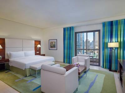 Chambre d'hôtel moderne avec lit double, coin salon et grande fenêtre donnant sur la ville.