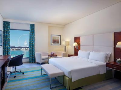 Chambre d'hôtel moderne avec grand lit, bureau, chaise et vue sur la mer par la fenêtre.