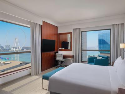 Modernes Hotelzimmer mit Meerblick, großem Bett und Schreibtisch vor Fenster.