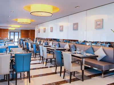 Modernes Restaurant mit blauen und weißen Stühlen, Tischen und großen Deckenleuchten.