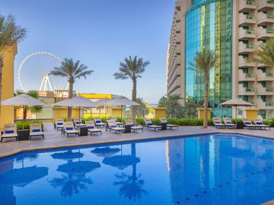 Moderner Hotelpool mit Liegen, Sonnenschirmen und Palmen, Hochhaus im Hintergrund.