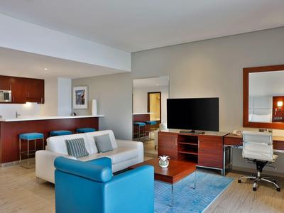 Moderner Hotelzimmer-Livingroom mit blauer Couch, Schreibtisch und Küchenzeile im Hintergrund