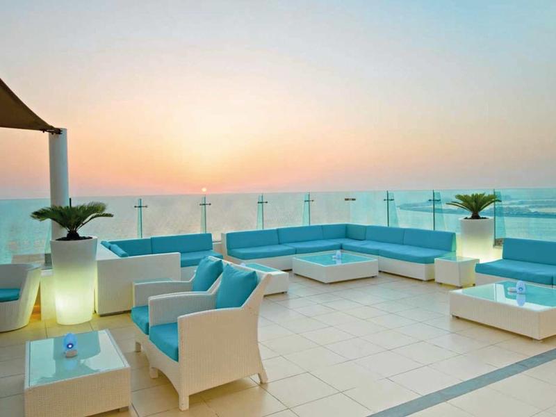 Terrasse sur le toit moderne avec meubles blancs et rambarde en verre au coucher du soleil.