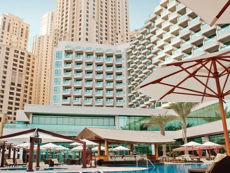 Piscine d'hôtel moderne avec chaises longues et parasols entourée de hauts bâtiments.