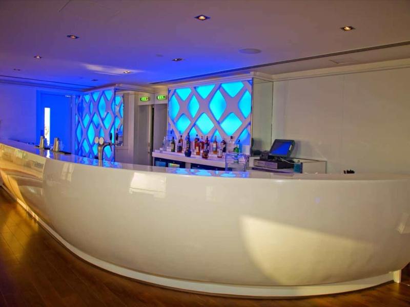 Espace de bar d'hôtel blanc moderne incurvé avec fond éclairé en bleu.