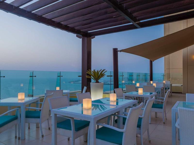Terrasse du soir avec tables dressées et vue sur la mer au crépuscule.