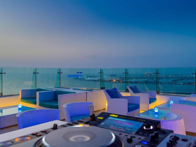 Terrasse sur le toit avec pupitre DJ, salon moderne et vue sur la mer au crépuscule.