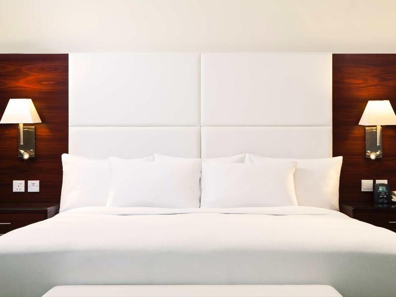 Grand lit d'hôtel avec linge de lit blanc et deux lampes murales sur panneaux en bois foncé.