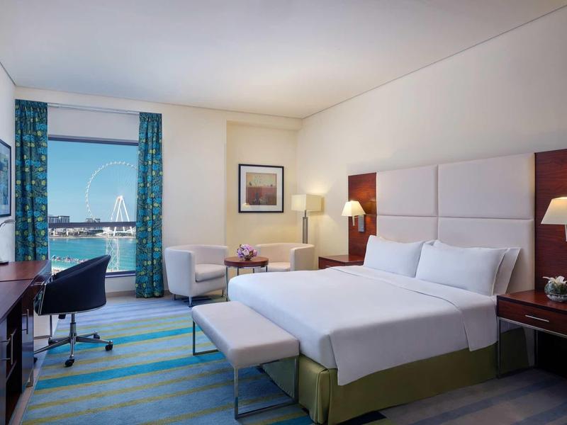 Chambre d'hôtel moderne avec grand lit, bureau, chaise et vue sur la mer par la fenêtre.