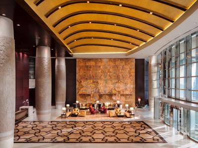 Große, helle Hotellobby mit gelber Gewölbedecke, Teppichmuster und bodentiefen Fenstern.