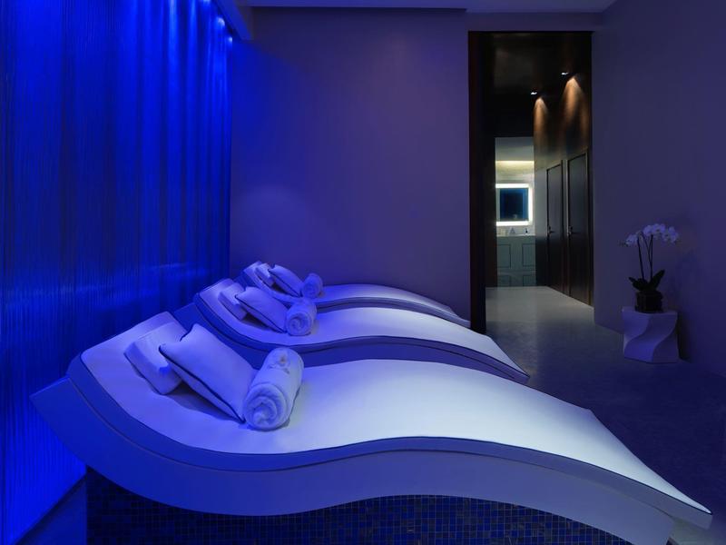 Dunkler Wellnessraum mit blauen LED-Lichtern, weißen Liegen und zusammengerollten Handtüchern.