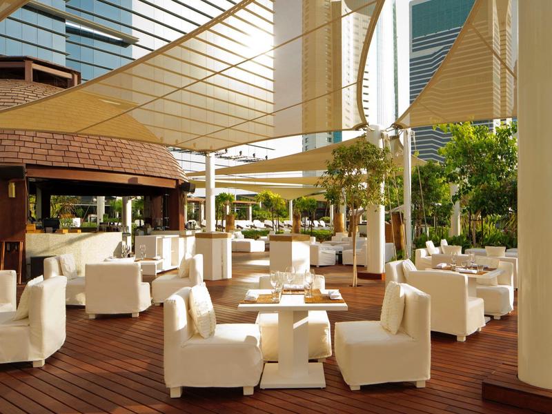 Moderner Außenbereich mit weißen Sitzmöbeln auf Holzboden und großen Sonnensegeln.