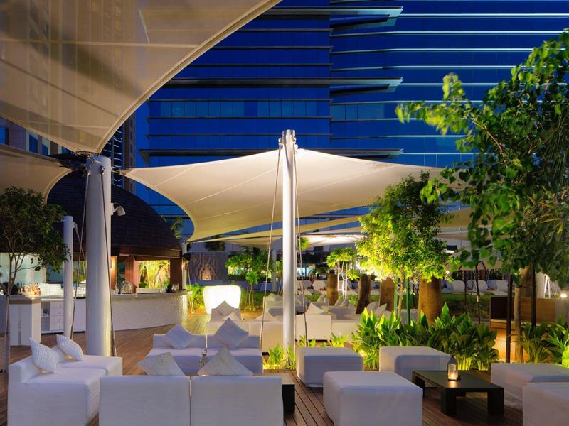 Moderner Außenbereich mit weißen Sitzmöbeln, Pflanzen und stilvoller Beleuchtung bei Abenddämmerung.