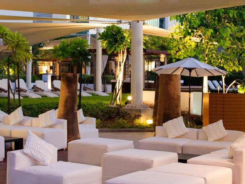 Moderne Lounge mit weißen Sofas, grünen Pflanzen und stilvoller Beleuchtung im Außenbereich.