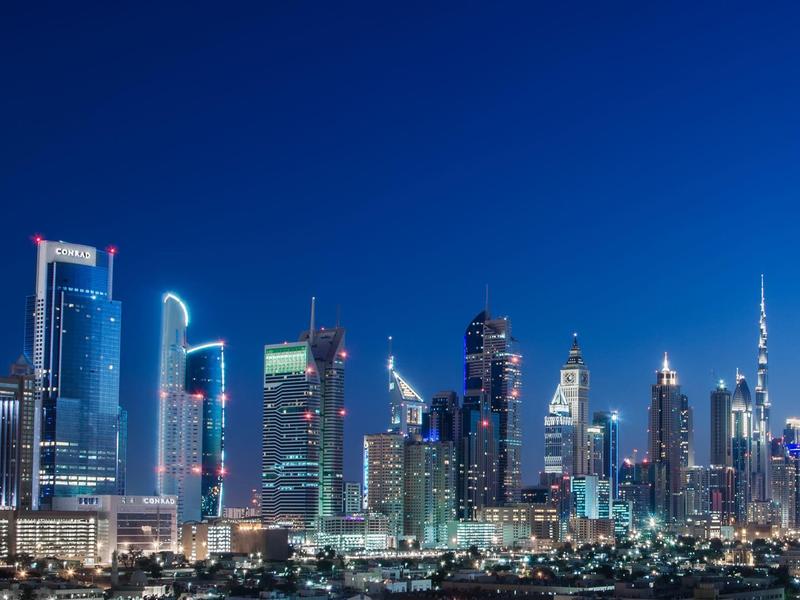 Nächtliche Stadtansicht mit beleuchteten Wolkenkratzern und klarem blauem Himmel.