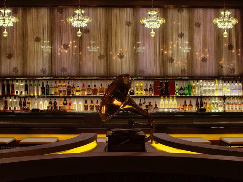 Elegante Bar mit dunklem Holz, Kronleuchtern und einer sitzenden Bronzestatue in der Mitte.