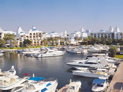 Marina s jachtami před bílými hotelovými budovami pod jasnou oblohou.