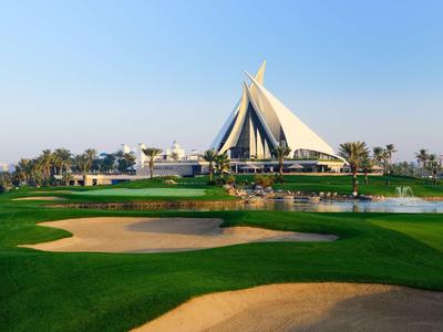 Green golf course with sand bunkers and a modern white pointed building in the background.