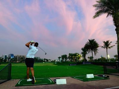 Person hitting golf ball on driving range at sunset with palm trees in the background