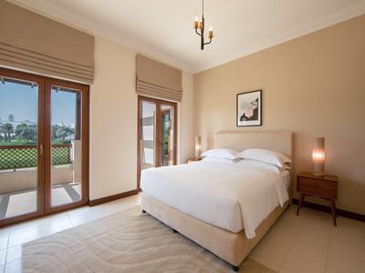 Světelná ložnice s manželskou postelí, nočními lampičkami a přístupem na balkon s výhledem do zahrady.