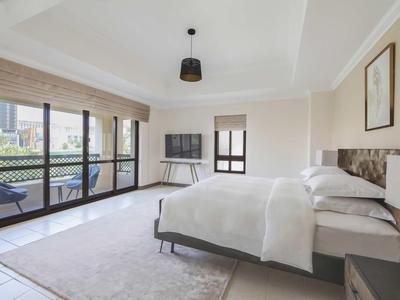 Světý hotelový pokoj s manželskou postelí, televizí, balkonem a moderním minimalistickým stylem.