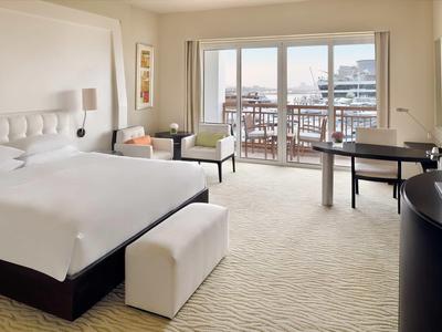 Moderní hotelový pokoj s velkou postelí, posezením a balkonem s výhledem na město.