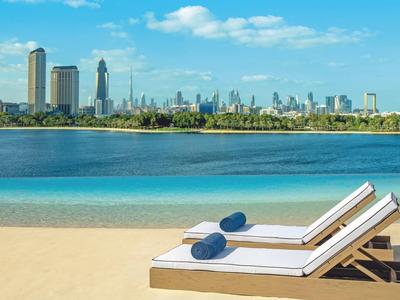 Dvě lehátka s modrými polštáři na písečné pláži s výhledem na městskou oblohu a modrou oblohu.