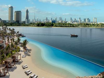 Ein künstlicher Strand mit Liegestühlen und Palmen am Fluss, im Hintergrund eine Stadtsilhouette.