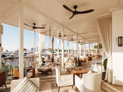 Open terrace with tables, chairs, ceiling fans, and a view of boats in the harbor.