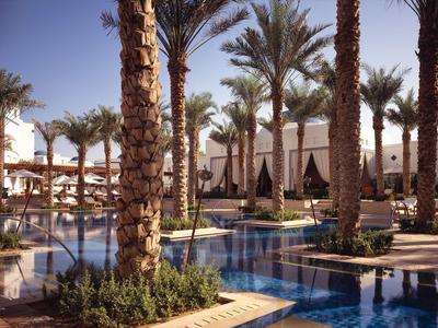 Luxusní bazénová oblast hotelového resortu s palmami a slunečníky pod jasnou oblohou.