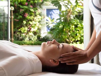 Žena dostává masáž hlavy v světlé místnosti s výhledem na zahradu.