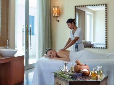 Žena dostává masáž v světlé místnosti s velkými okny a dekorativními prvky.