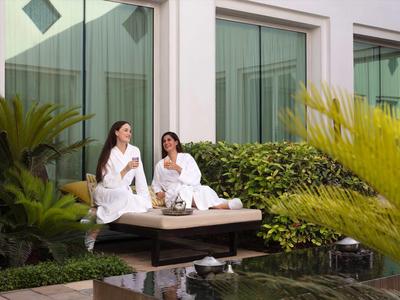 Dvě ženy v županech sedí v hotelové zahradě a užívají si nápoje v klidném prostředí.