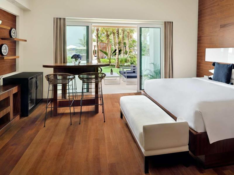 Moderní hotelový pokoj s manželskou postelí, dřevěnou podlahou a výhledem na zahradu a bazén.